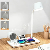 A white multi-functional desk lamp and charging station set on a wooden desk, featuring a flexible LED lamp, a built-in speaker, a digital alarm clock, and a wireless charging pad with a smartphone placed on top. The image includes three inset images on the left showing the lamp in different angles, and musical note graphics indicate sound output.