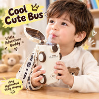 A young child drinking from a cute toy-like water bottle shaped like a small bus, with a strap hanging around the wrist. The scene is indoors with a blurred teddy bear and bookshelf in the background, plus decorative text overlays reading 'Cool Cute Bus' and 'Little Adventure Buddy'.