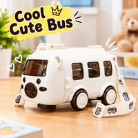 A white toy bus with dark brown windows and wheels, featuring a matching printed carrying strap, displayed on a wooden table with a blurred teddy bear and indoor background. A yellow graphic overlay reads 'Cool Cute Bus'.