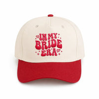 Two-tone cream and red custom embroidered cap with 'IN MY BRIDE ERA' text and hearts.