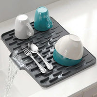 Multiple plates bowls and glasses arranged neatly on top of the silicone dish drying mat