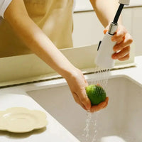 Person washing a lime under a white kitchen faucet spray in a white sink.
