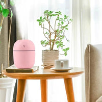 Pink humidifier on a wooden table with a plant and cup in a bright room