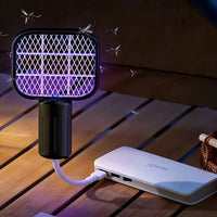 A mosquito trap light with a black grid and glowing purple UV light, shown plugged into a white power bank on a wooden table, with illustrated mosquitoes flying around.