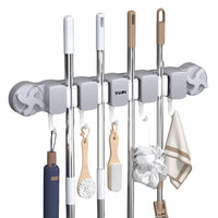 A Yopi wall-mounted multi-tool broom holder with five adjustable slots holding various cleaning tools including brooms, a duster, a scrubber, and a towel, shown against a solid white background.