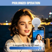 A woman at night uses a smartphone selfie-style video call with a small circular clip-on light attached to the phone. The image includes marketing text reading 'PROLONGED OPERATION' and 'It remains on for up to 1 hour.