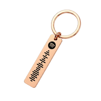 A rose gold keychain featuring a rectangular bar engraved with a Spotify logo and sound wave, attached to a split key ring on a solid white background.